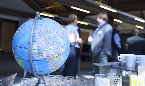 Close up of a globe focused on Europe and Africa, with a group of people in business attire conversing in the blurred background of a modern indoor setting.